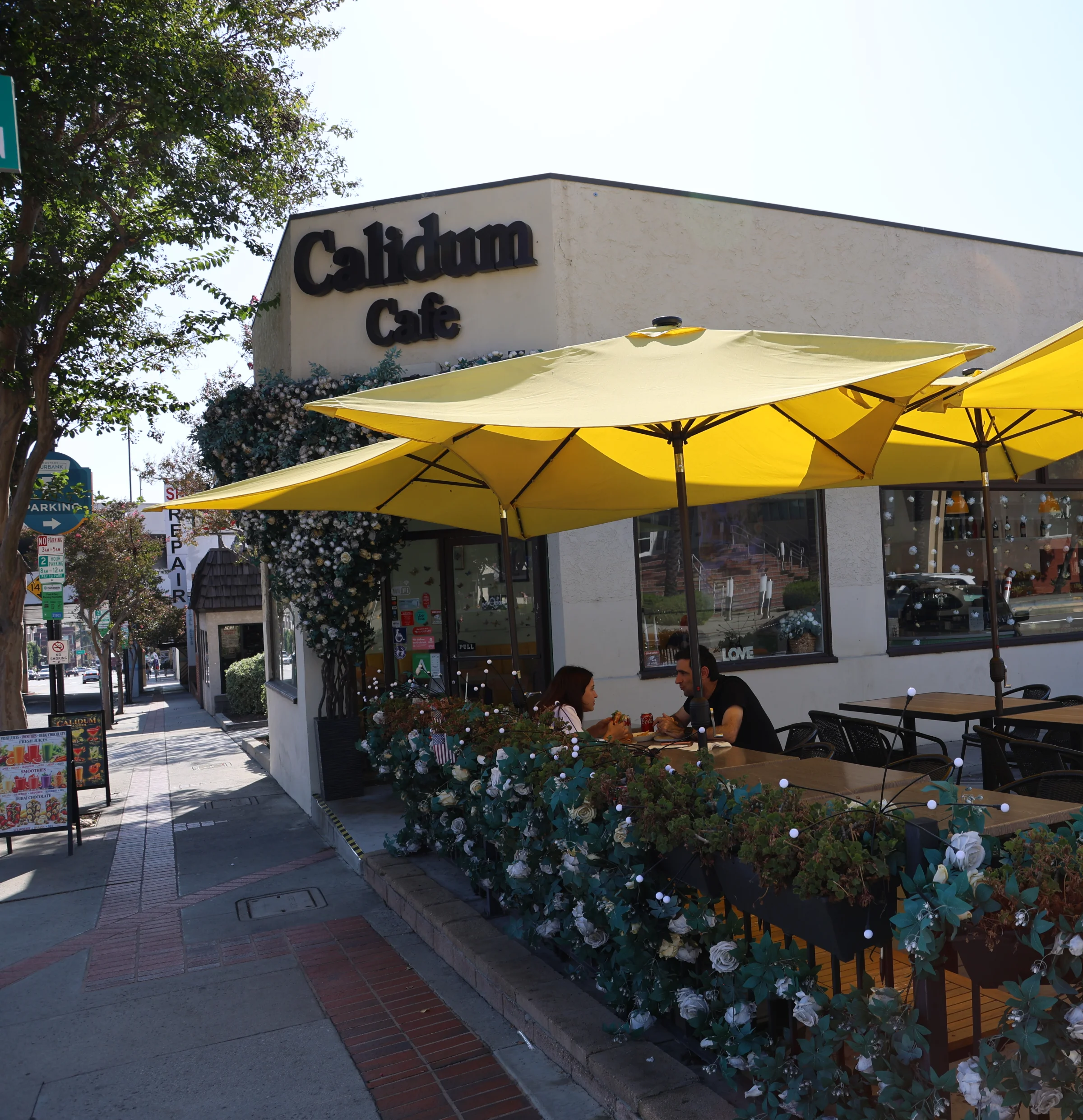 Sidewalk seating under yellow umbrellas at Calidum Cafe